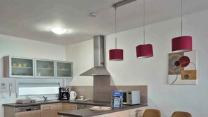 A modern kitchen with a central island, a dining area with chairs, and pendant lights. - Holiday apartment with pool Wi-Fi and tasteful decoration (Siófok)