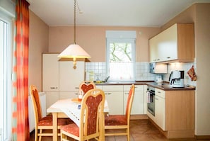 Cozinha compacta com mesa de jantar, cadeiras, luminária pendente e janela com vista.