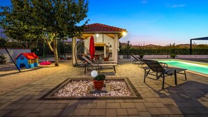 Ein Patio-Bereich mit Pool, Liegestühlen, einem Spielhäuschen und einer Pergola.