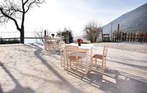 Une terrasse extérieure avec une table et des chaises, un pot de fleurs et une vue sur un lac et des montagnes.
