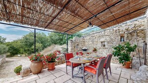 Un patio al aire libre con pared de piedra, mobiliario de mimbre y plantas en macetas.
