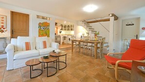 Una sala de estar con sofá, mesa de centro y una silla roja. Se aprecia una cocina al fondo, con mesa y sillas para comer.