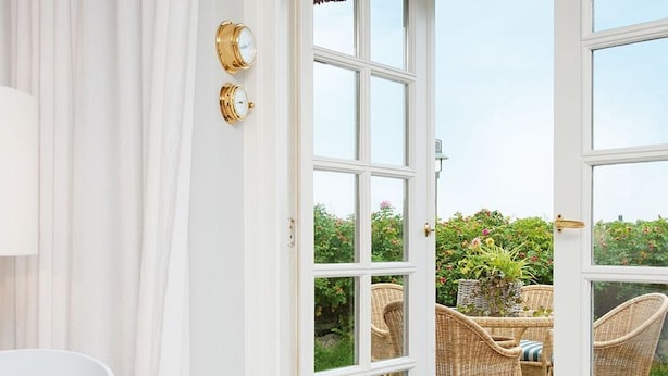 Habitación con una puerta blanca que da a un patio exterior con mobiliario de mimbre y vistas a un jardín.