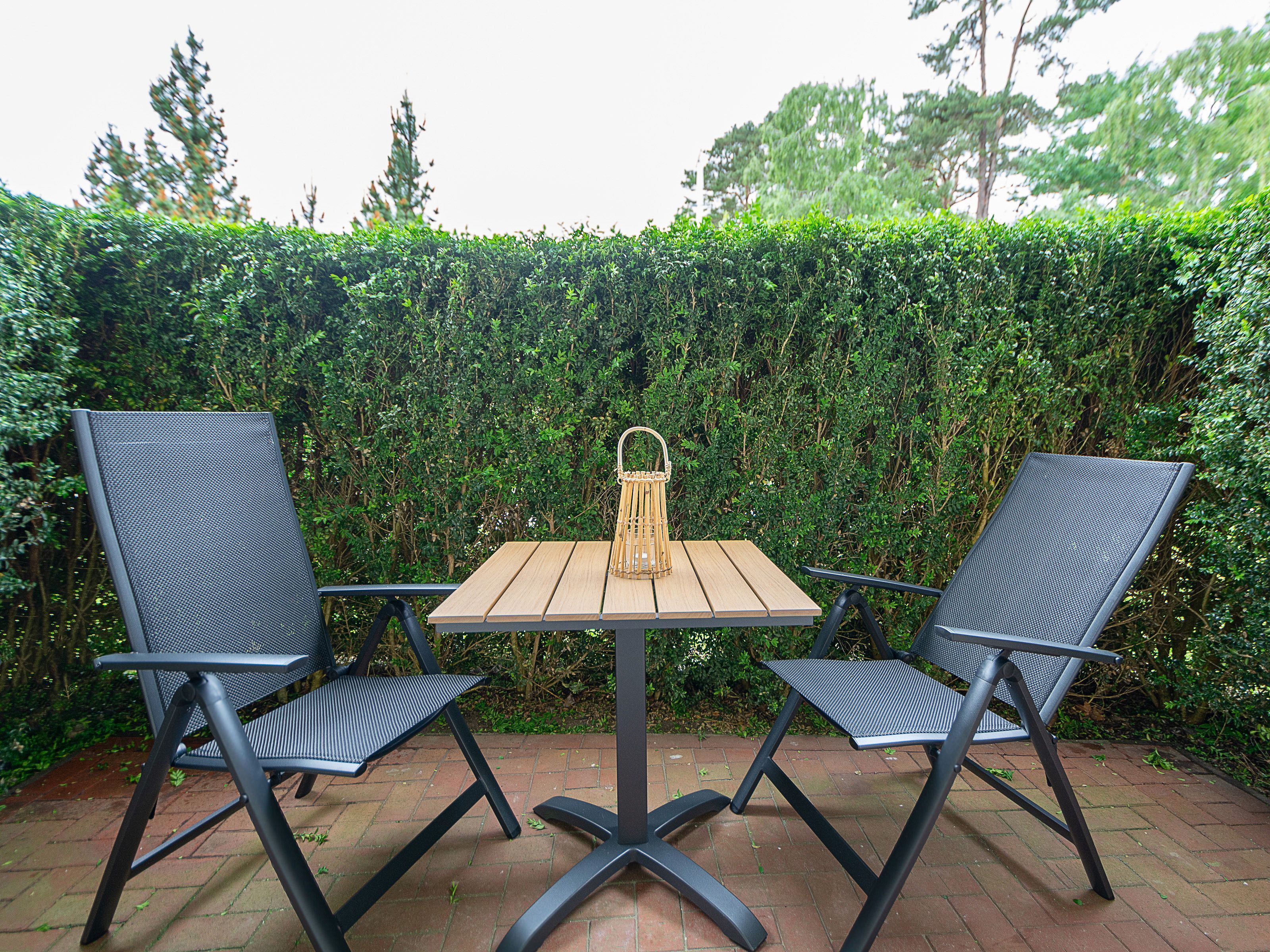 A patio with two chairs and a table, surrounded by a hedge.