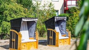 Two wooden beach chairs with mosquito netting, positioned on sandy ground with dense greenery in the background. - Dune garden Whg. Wa45-31 - Wa45-31 (Kühlungsborn)