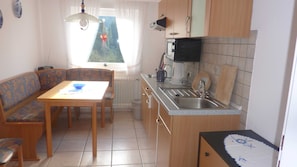A compact kitchen with a dining area, including a table, chairs, and a microwave. - Apartment 9 - Apartment Brüggemann (Altenau)