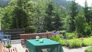 An outdoor patio with a wooden bench and a table covered with a green tablecloth.