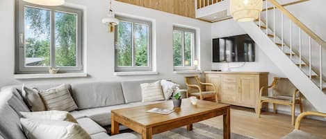 Amplia sala de estar con techo de madera, ventanas grandes, un sofá, una mesa de centro y una escalera.