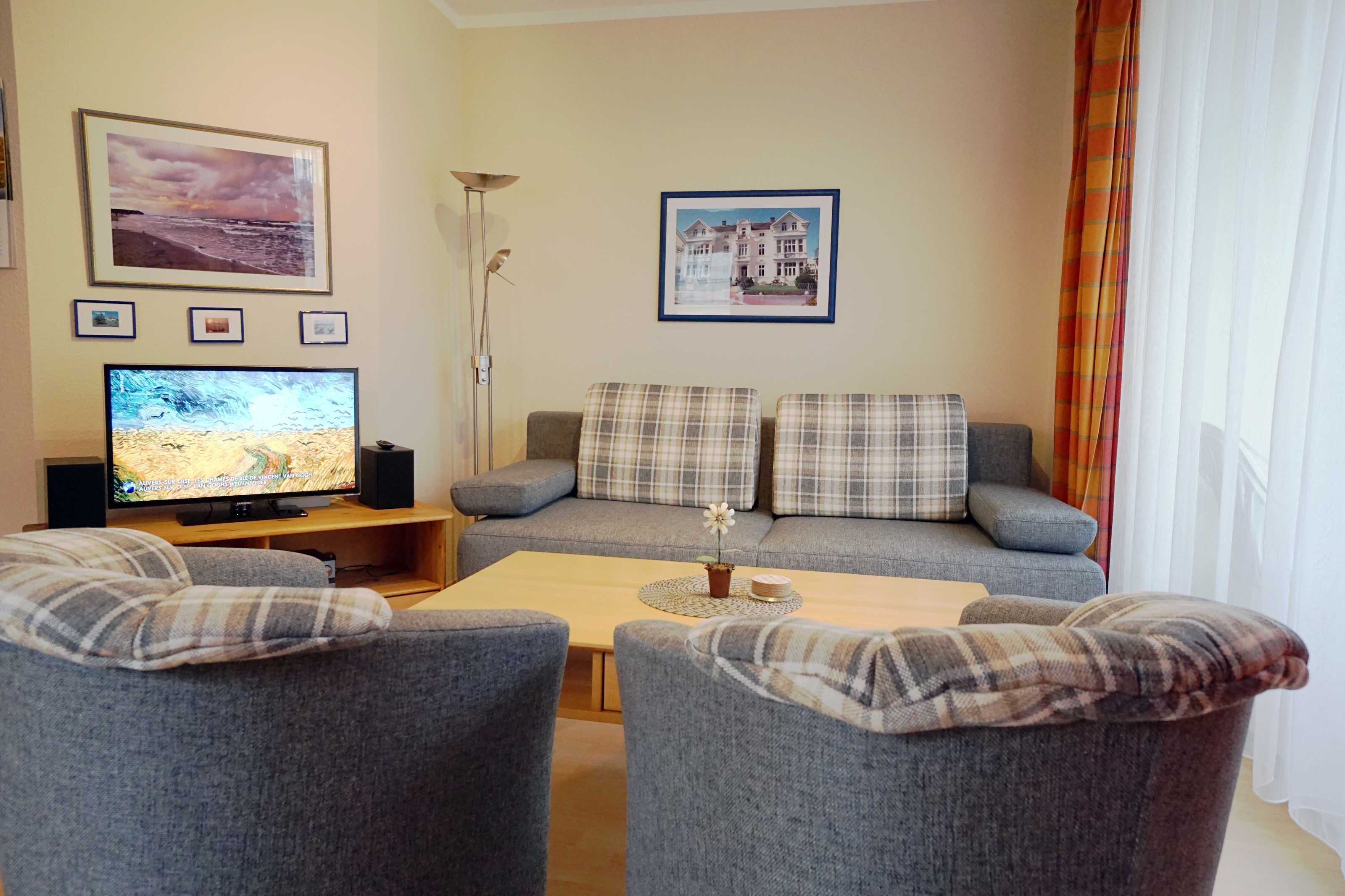 A living room with a grey sofa, two armchairs, a coffee table, a flat-screen TV, and framed pictures on the wall.