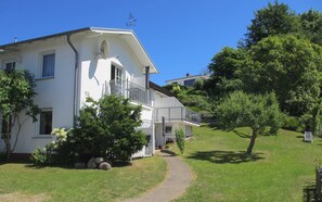 Un edificio bianco a due piani con un balcone, immerso nel verde e sotto un cielo sereno.