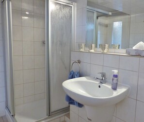 Un bagno con cabina doccia in vetro, un lavandino bianco con uno specchio sopra e uno scaffale con contenitori in vetro.