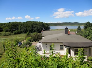 A house with a large roof, a chimney, and a view of a lake and forest.