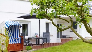 A patio area with a striped umbrella, a table with bowls, and a white building in the background. - 1-room apartment on the ground floor with south-west facing terrace - Ferienhaus am Schmachter See (Binz)