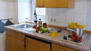 A kitchen with a sink, countertop, and wooden cabinets. - 1-room apartment on the ground floor with south-west facing terrace - Ferienhaus am Schmachter See (Binz)