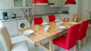 Eine moderne Küche mit weißen Schränken, einem Holzespeisetisch für vier Personen, roten Stühlen und Pendelleuchten.