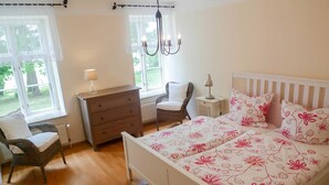 Ein Schlafzimmer mit einem Bett, zwei Stühlen, einer Kommode, einem Nachttisch und einer Pendelleuchte.