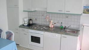Een kleine keuken met witte kastjes, een inbouwoven, een vaatwasser en een koffiezetapparaat.