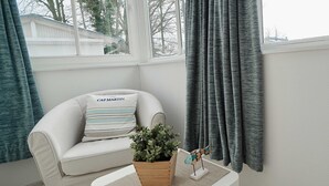 A corner of a room with a white sofa, a wooden side table, a potted plant, and a small decorative fish. - Ferienappartement Mönchgut (A) - Apartment house "Haus Arkona" (Sellin)