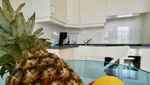 A pineapple on a glass table in a kitchen with white cabinets and a coffee maker. - Ferienappartement Mönchgut (A) - Apartment house "Haus Arkona" (Sellin)