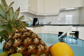Una piña sobre una mesa de vidrio en una cocina con armarios blancos y una cafetera.