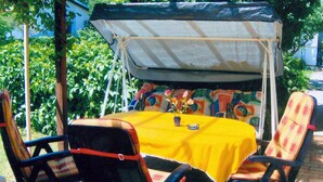 An outdoor patio with a table covered by a yellow tablecloth, surrounded by chairs with plaid cushions.