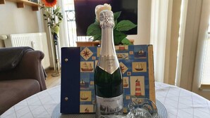 Eine Champagnerflasche auf einem Tisch mit Unterlage, umgeben von einer schiffs-inspirierten Schachtel und einem dekorativen Glas.