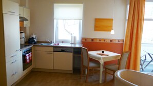 A compact kitchen with a dishwasher, oven, and a dining area with a table and chairs. - App. 1 - Hühnergott - Villa Am Steinbach in the historic center - 150m to the Baltic Sea (Sassnitz)
