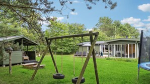 A wooden swing set with tire swings in a grassy backyard, surrounded by two wooden cabins with attached porches. - 3 bedroom beach front home in Højby (Højby)