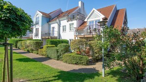 Een groot, twee verdiepingen tellend huis met een dak van rode tegels, een balkon en een verzorgde tuin met hagen en een pad.