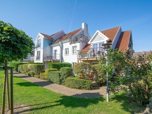 A large, two-story house with a red-tiled roof, a balcony, and a well-maintained garden with hedges and a pathway.
