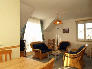 En hyggelig stue med et træbord, to fletstole med blå puder, et glasbord og en hængende lampe.