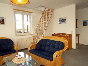 A living room with wicker furniture, a glass coffee table, a wooden staircase, and a view of the outside.