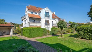 Een herenhuis met twee verdiepingen, een rood pannendak, een balkon en een verzorgde tuin met hagen en een pad.