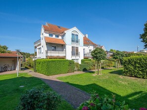A two-story house with a red-tiled roof, a balcony, and a well-maintained garden with hedges and a pathway.