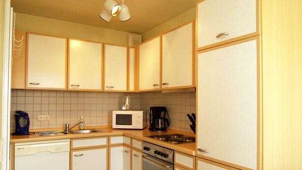 Een compacte keuken met witte kastjes, een magnetron, een koffiezetapparaat en een vaatwasser.