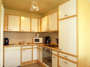 A compact kitchen with white cabinets, a microwave, a coffee maker, and a dishwasher.