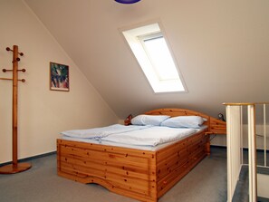 Une chambre avec un plafond en pente, un lit en bois, une petite table de chevet, un porte-manteau et un tableau accroché au mur.