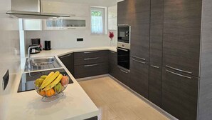 Une cuisine moderne avec des meubles de couleur sombre, des appareils en acier inoxydable et un panier de fruits posé sur le plan de travail.