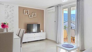 Un soggiorno moderno con televisione a schermo piatto, un divano, un tavolo da pranzo e un balcone con vista.
