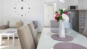 Un soggiorno moderno con tavolo da pranzo, divani, orologio e angolo cottura con elettrodomestici.