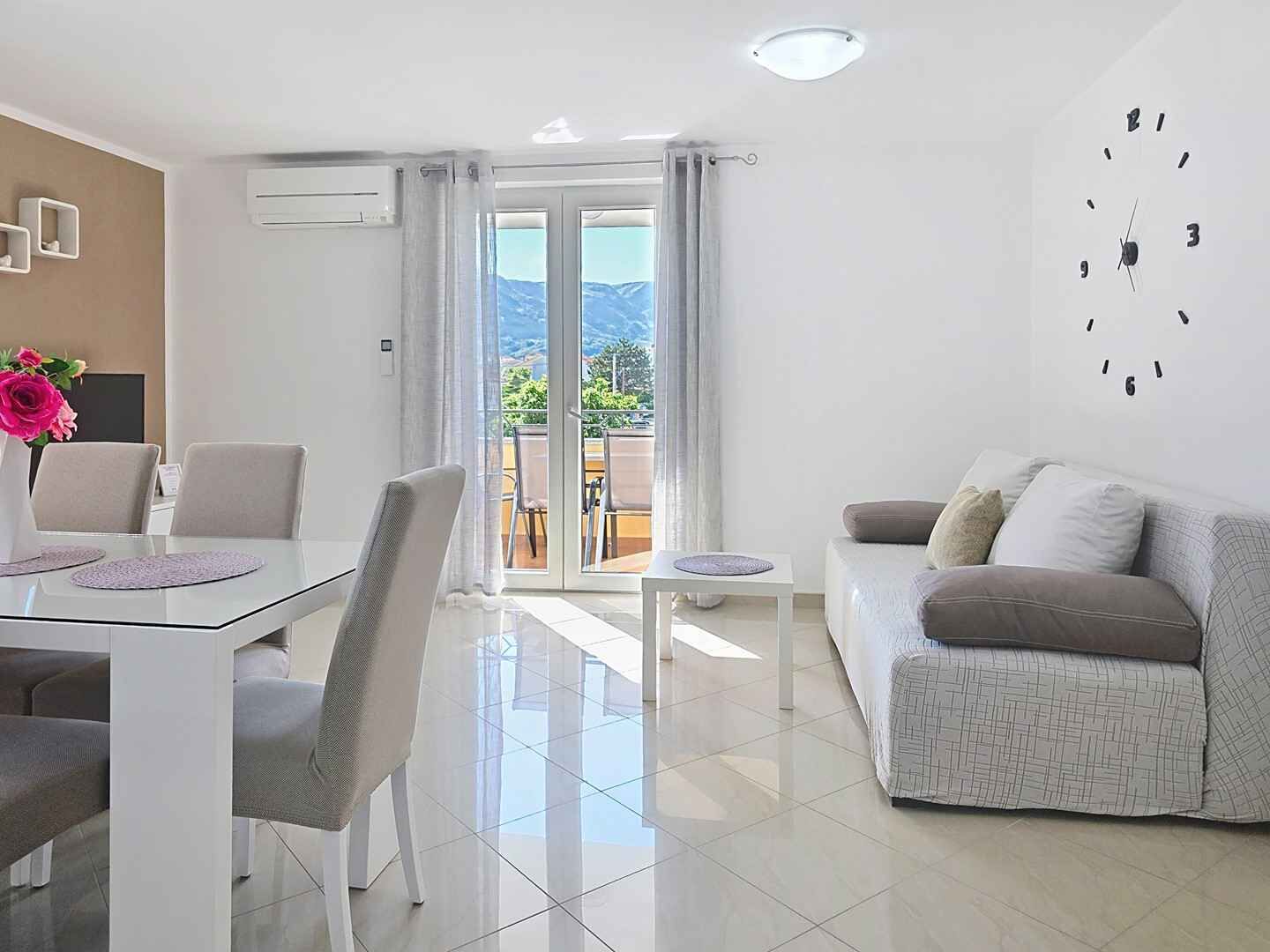 A modern living room with a dining area, a sofa, and a view of the outdoors.