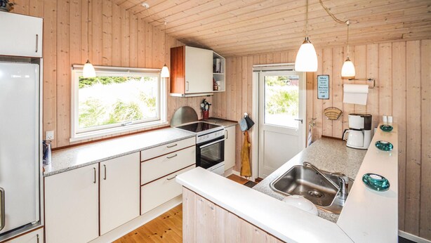 Una cucina compatta con pareti in legno, forno integrato, lavello e finestra che permette l'ingresso di luce naturale.
