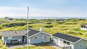 Una casa sul lungomare con tetto in metallo, circondata da dune erbose e vista libera sul mare.