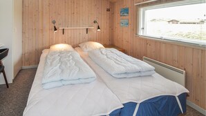 Un letto matrimoniale con piumone bianco e copriletto azzurro, pareti in legno, una finestra con vista e un tavolino con una lampada.