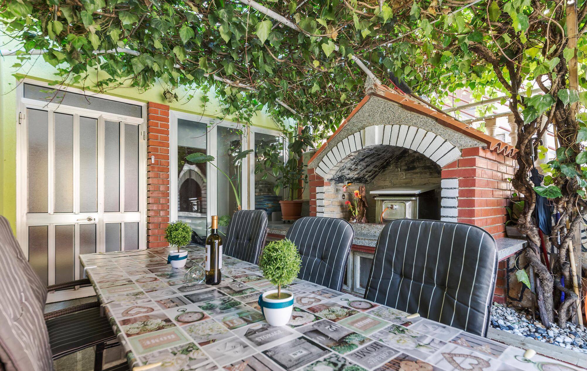 An outdoor dining area with a brick oven, striped chairs, and a table covered with a newspaper print tablecloth.