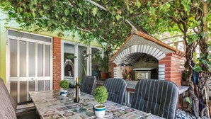 An outdoor dining area with a brick oven, striped chairs, and a table covered with a newspaper print tablecloth. - 2 bedroom cozy apartment in Pula (Pula)