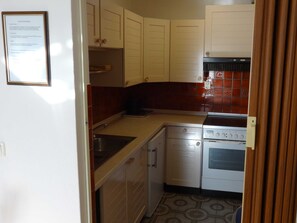 Una cocina compacta con armarios blancos, una estufa y un lavabo.