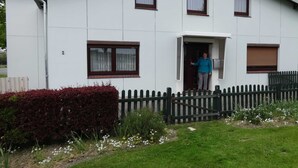 En tvåvåningsbyggnad med ett grönt tak, en liten veranda och ett trästaket.