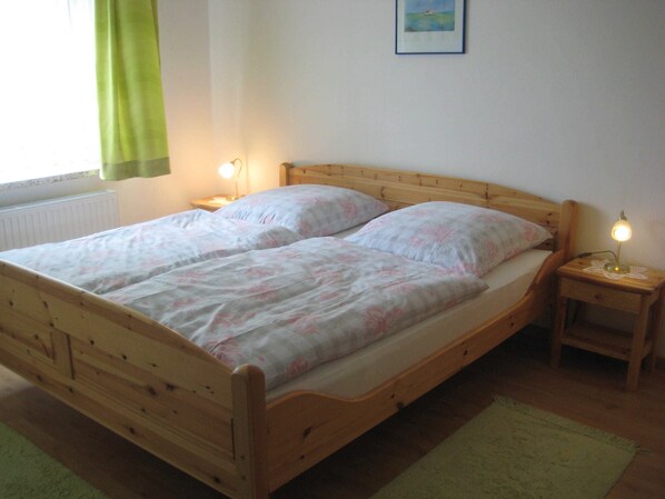 Una cama de madera con una colcha floral y dos almohadas, flanqueada por mesitas de noche con lámparas, en una habitación con un radiador y un cuadro en la pared.
