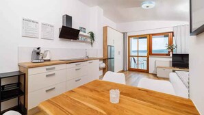 Una cocina moderna con armarios blancos, una mesa de comedor de madera y vista al mar a través de amplios ventanales.